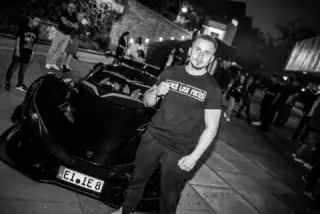 Kämpfer posiert vor einem Sportwagen bei einer Abendveranstaltung